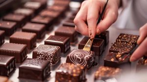 Gros plan sur une main d'artisan utilisant un pinceau pour décorer délicatement un chocolat artisanal avec des motifs dorés