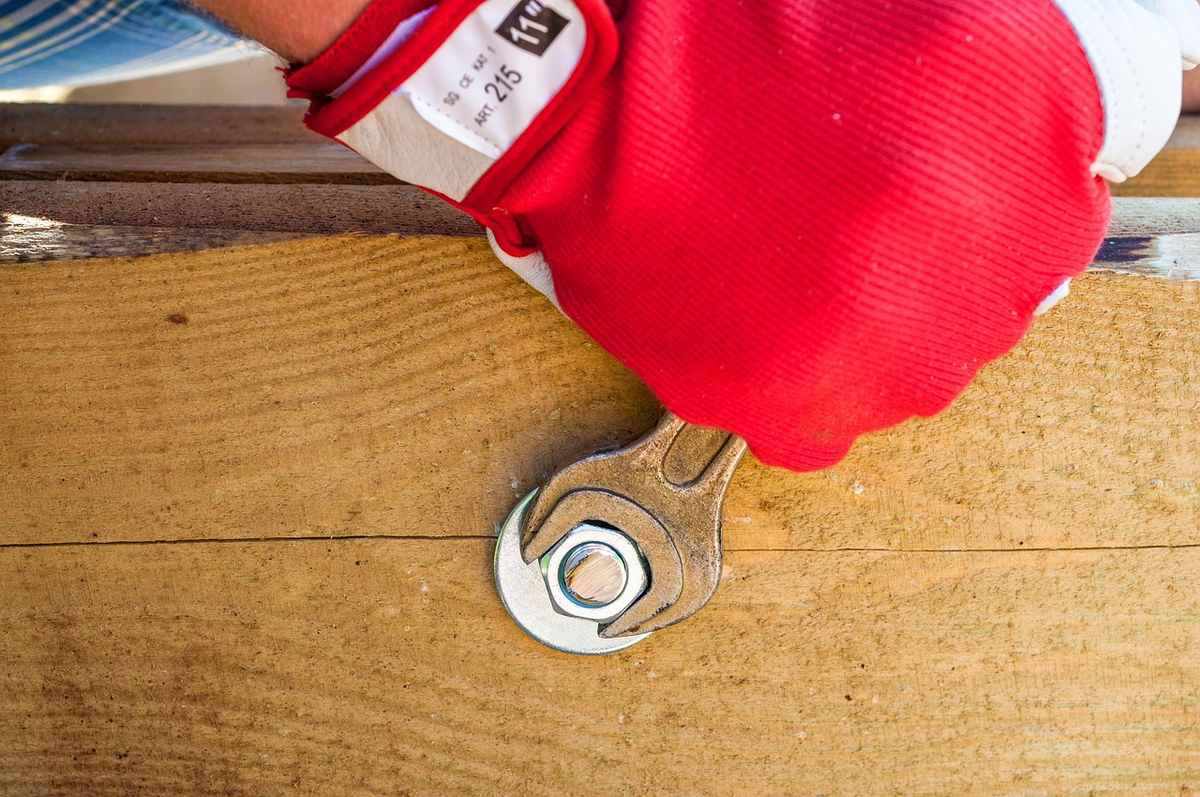 Une main gantée serre une vis avec une clé sur du bois