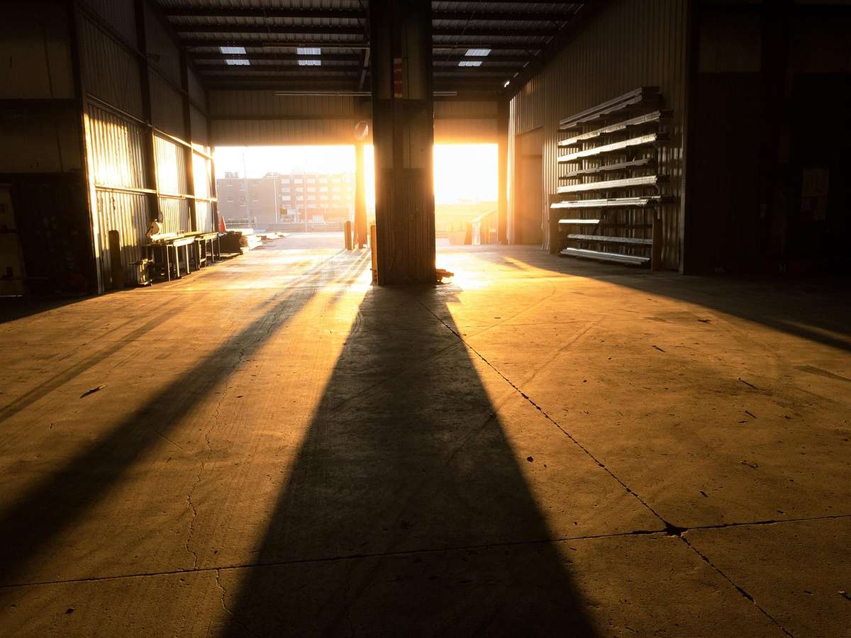 Lumière dorée inonde le hall industriel, projetant de longues ombres sur le béton