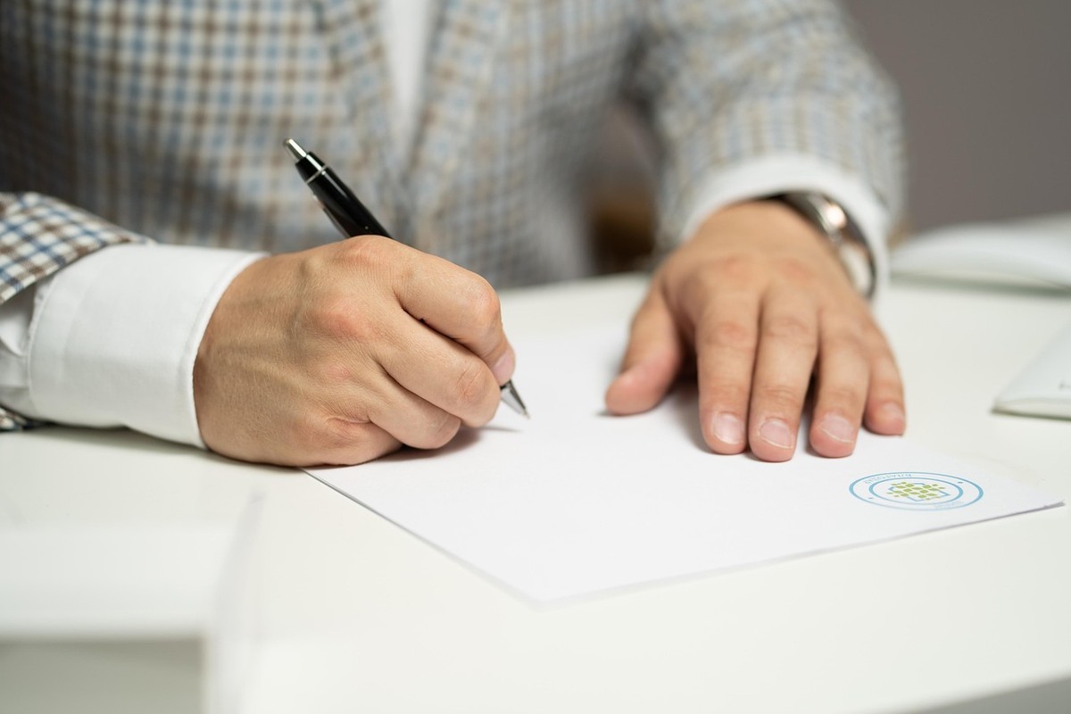 Un homme en chemise et veste trace une signature sur feuille